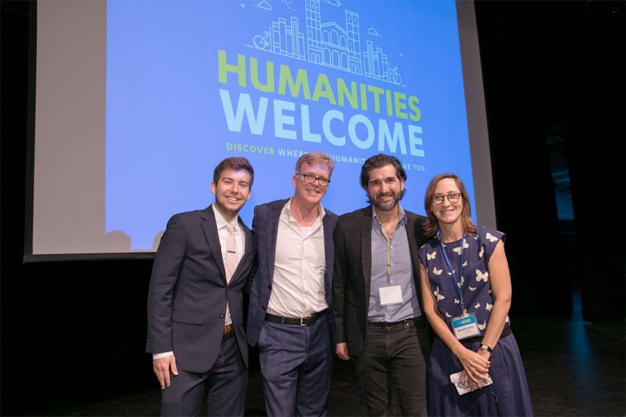 Four people smile against a Powerpoint backdrop