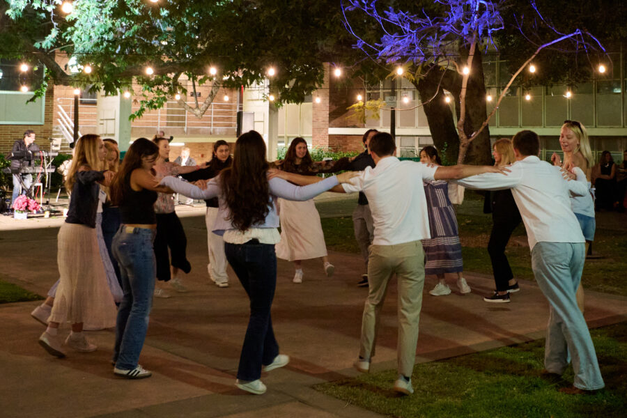 Group of people dancing in a circle at night under string lights