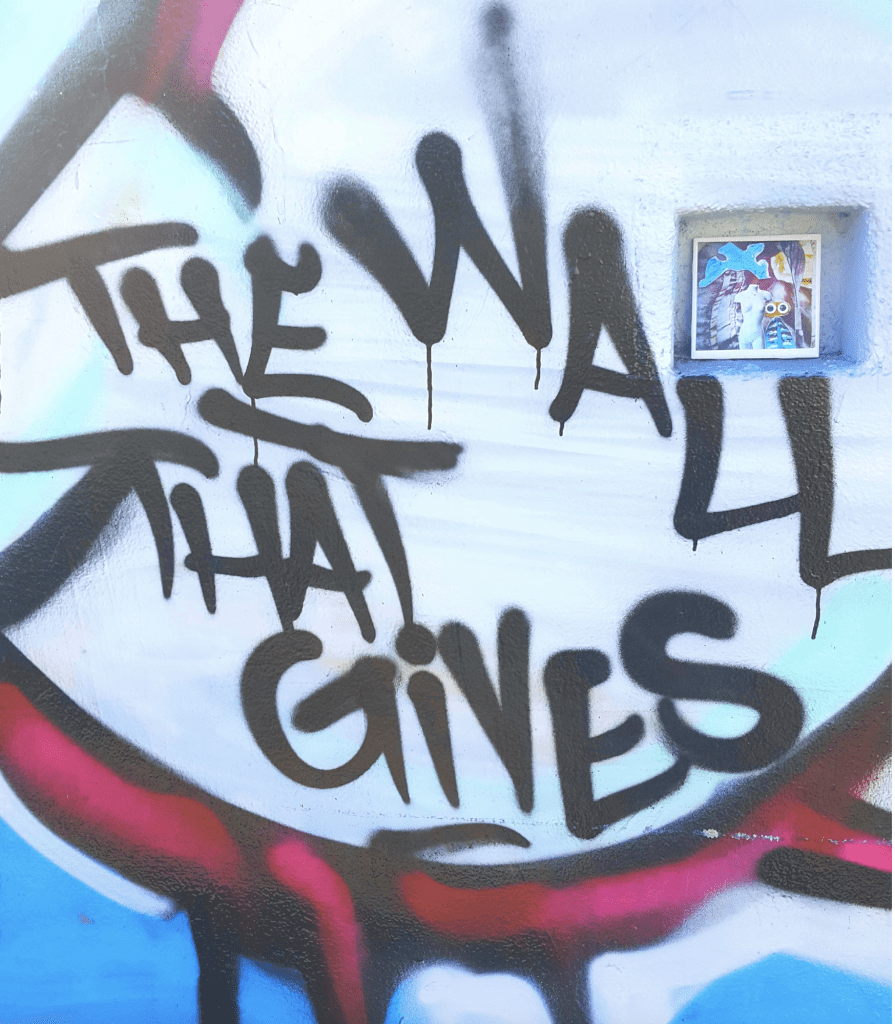 The phrase "The Wall that Gives" is painted on a white wall