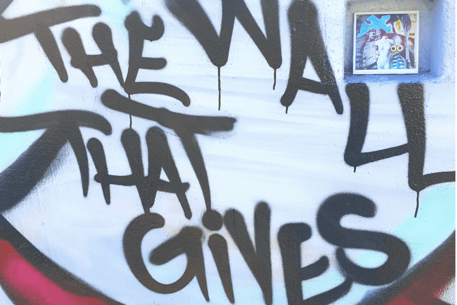 The phrase "The Wall that Gives" is painted on a white wall
