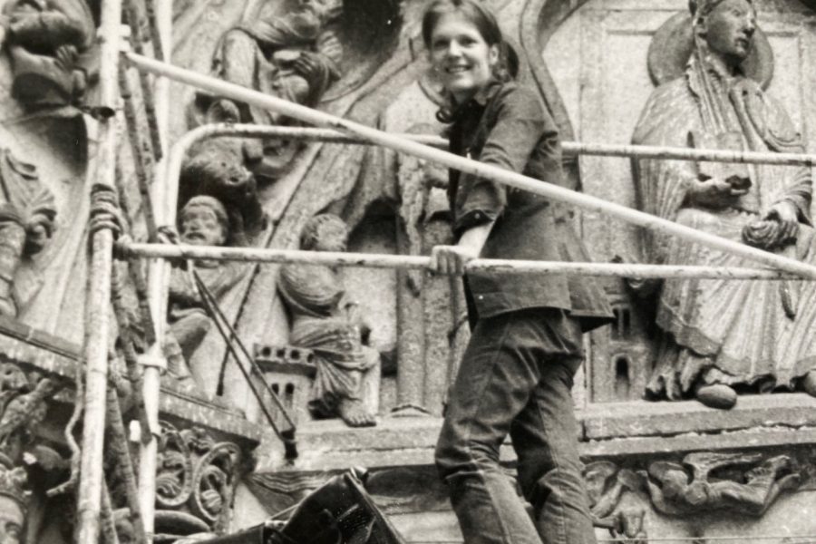 Diane Brouillette poses on some scaffolding by a stone relief in a black-and-white photo