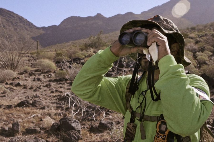 A man scans a desert landscape with binoculars