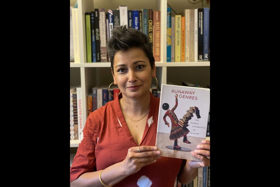 Yogita Goyal poses with her book against a bookshelf.