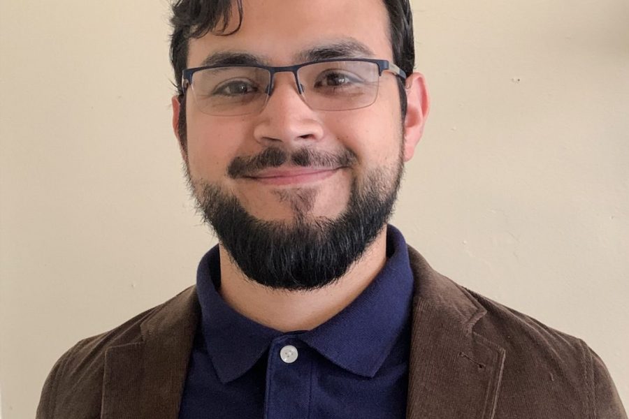 Julio Vega-Payne smiles against a tan backdrop