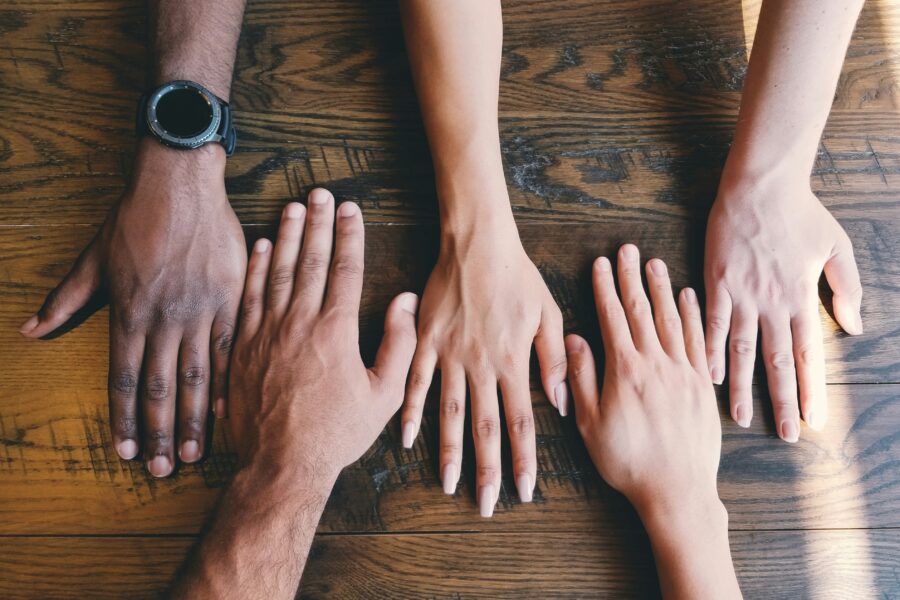 Five hands with different skin tones on a wooden table