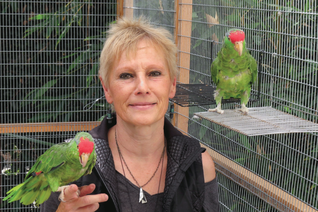 Portrait of Ursula Heise with one parrot on her hand and another next to her