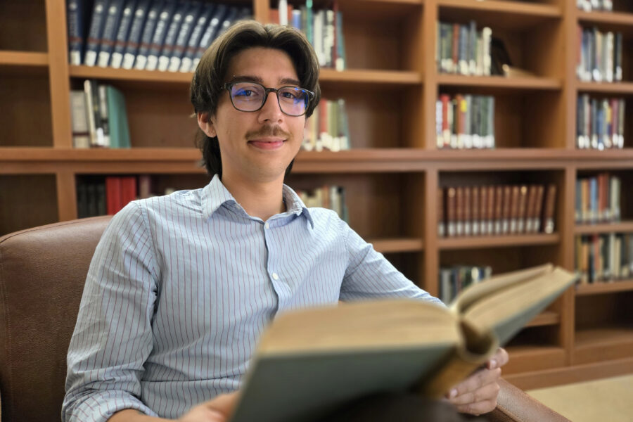 Eric Sican seated in leather chair with bookshelves behind him