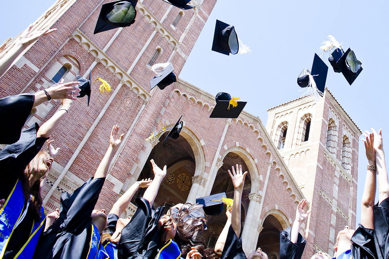 UCLA graduates tossing their caps into the air for commencement with Royce Hall in the background