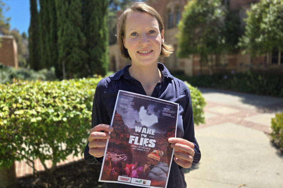 Lena Trüper standing outdoors holding a flyer for "Wake the Flies," a documentary she produced