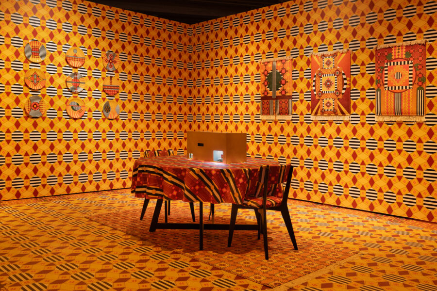 Installation at MASS MoCA featuring AI-assisted tasseography readings, brass enclosure, Armenian patterns on wall paper, flooring, textiles and ceramics, with furniture, and books