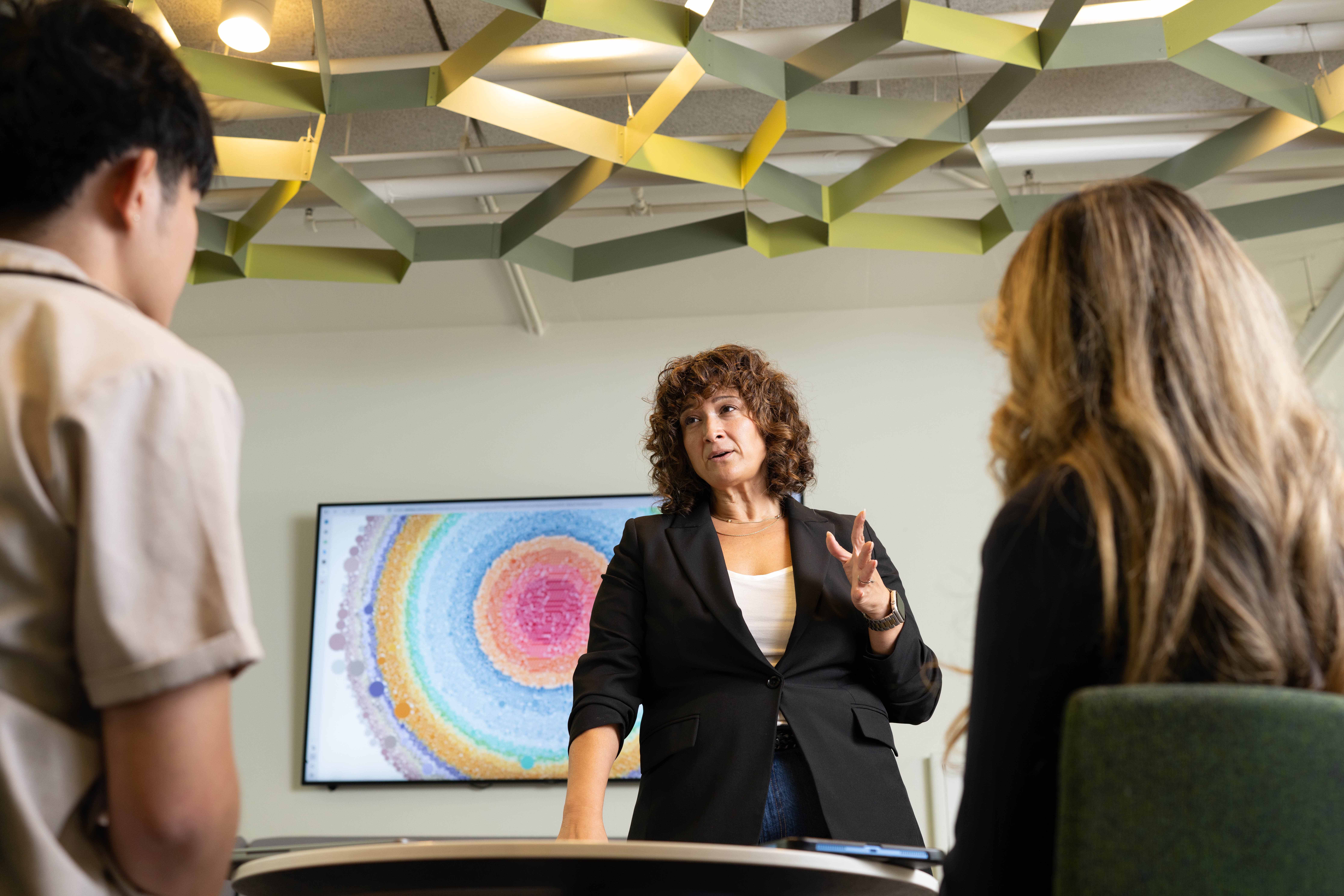 UCLA lecturer Wendy Kurtz with multicolored digital visualization behind her; backs of students' heads in foreground