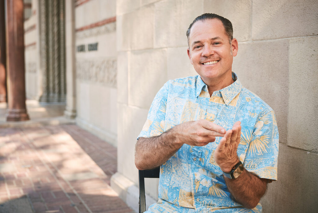 Benjamin Lewis outside of Powell Library displaying the ASL sign for the word "integrity"