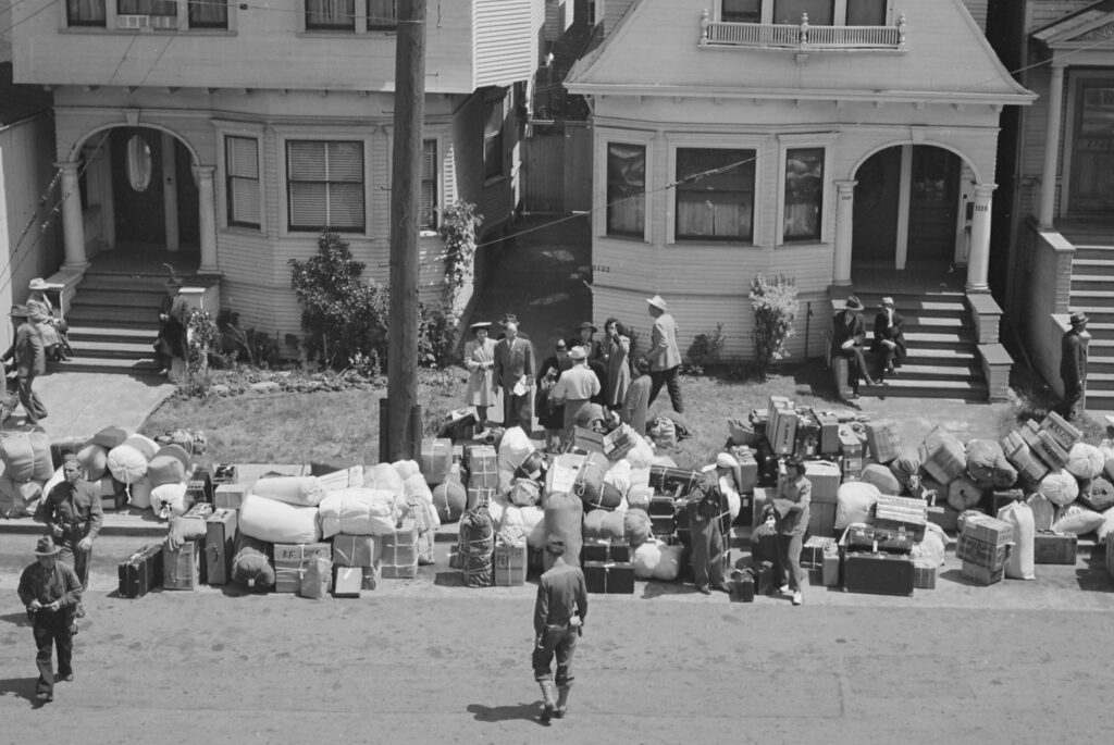 Black and white photo of personal belongings stacked on sidewalk in front of homes