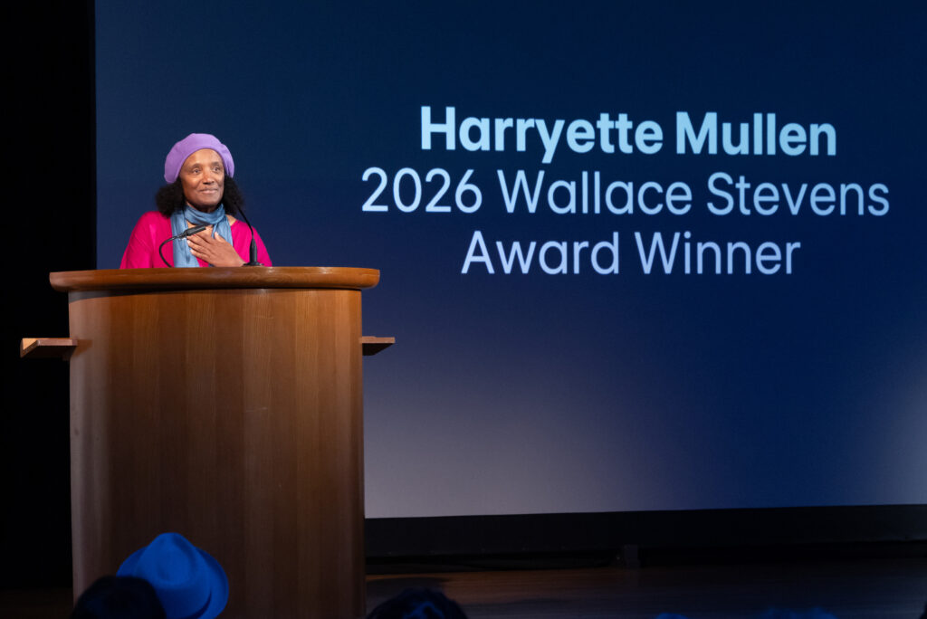 Harryette Mullen on stage behind lectern with her name and name of poetry award on screen behind her