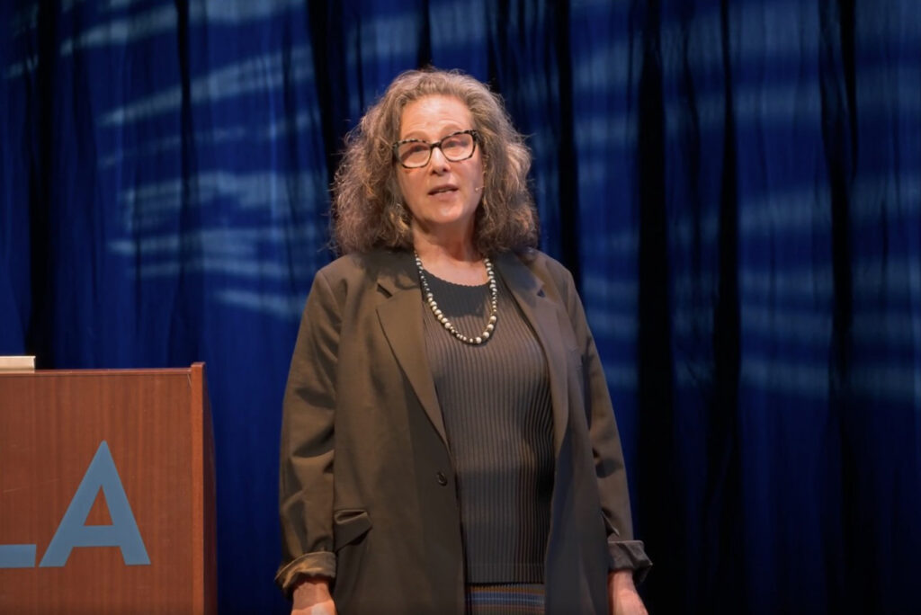 Helen Deutsch speaking with dark screen in background and UCLA lectern beside her