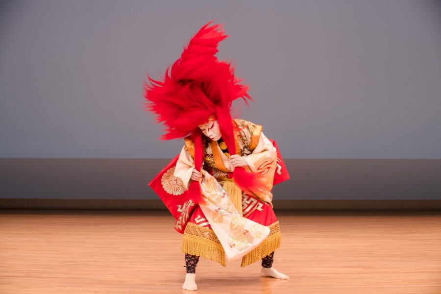 Kabuki performer wearing large red headdress and traditional robe on a stage